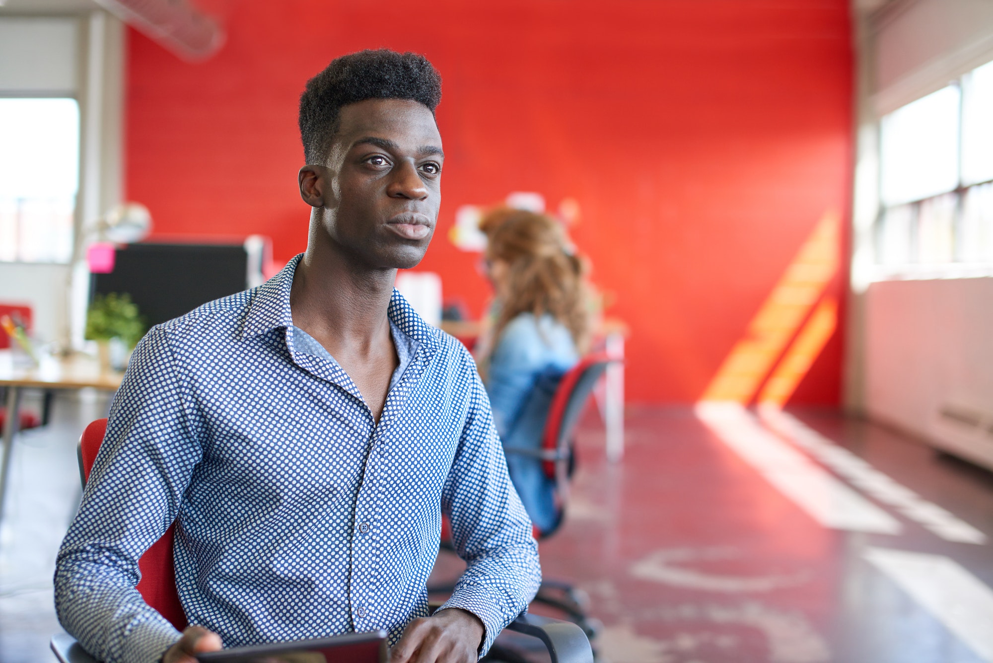 Confident male designer working on a digital tablet in red creative office space