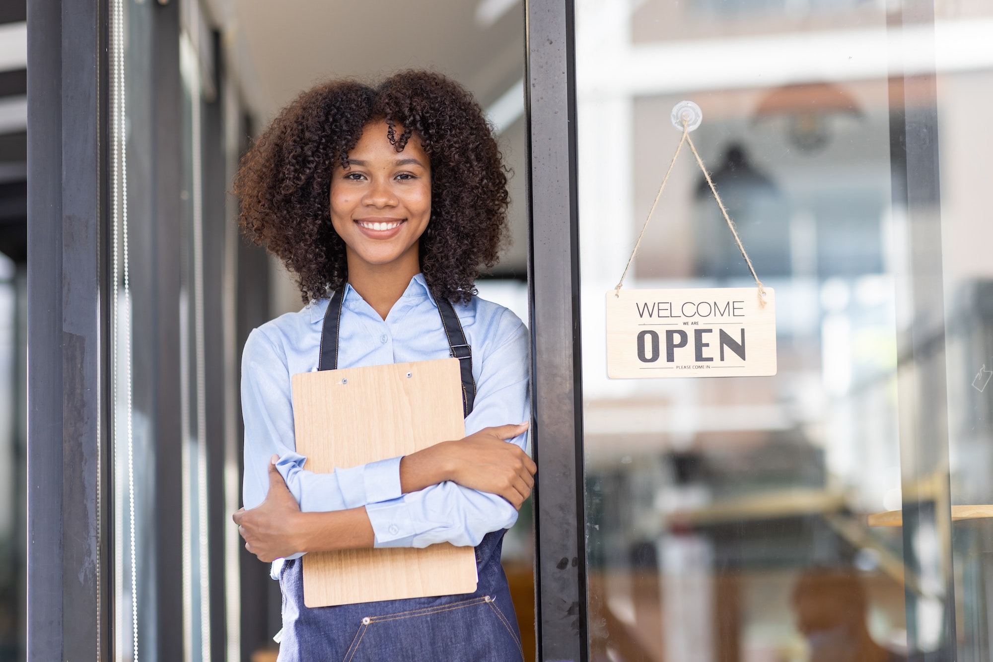 Happy waitress standing at restaurant entrance. Portrait of african american business woman attend